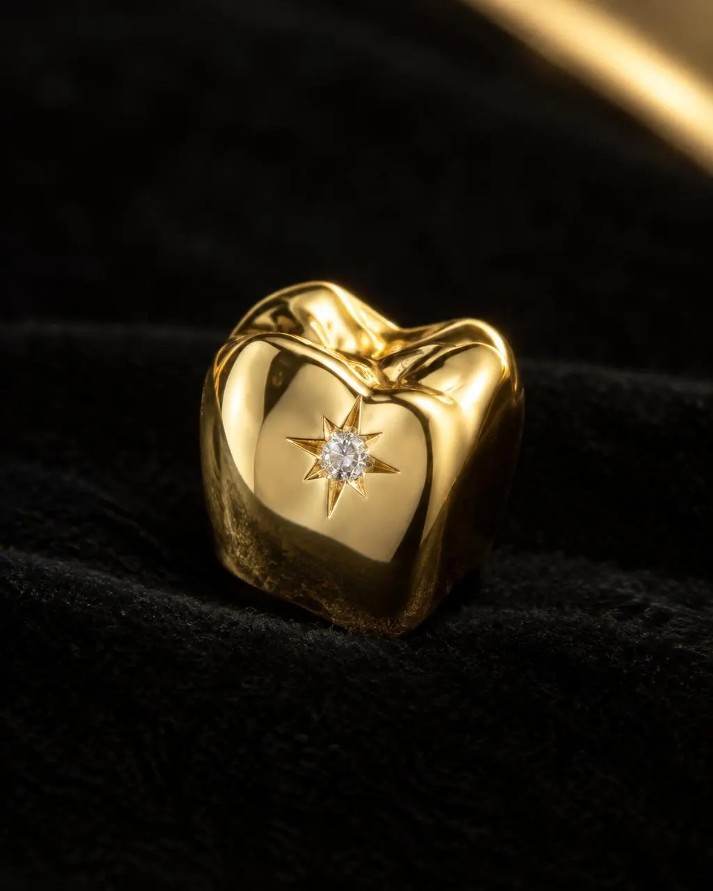 Single 14K yellow gold tooth cap with a star-set diamond on black velvet